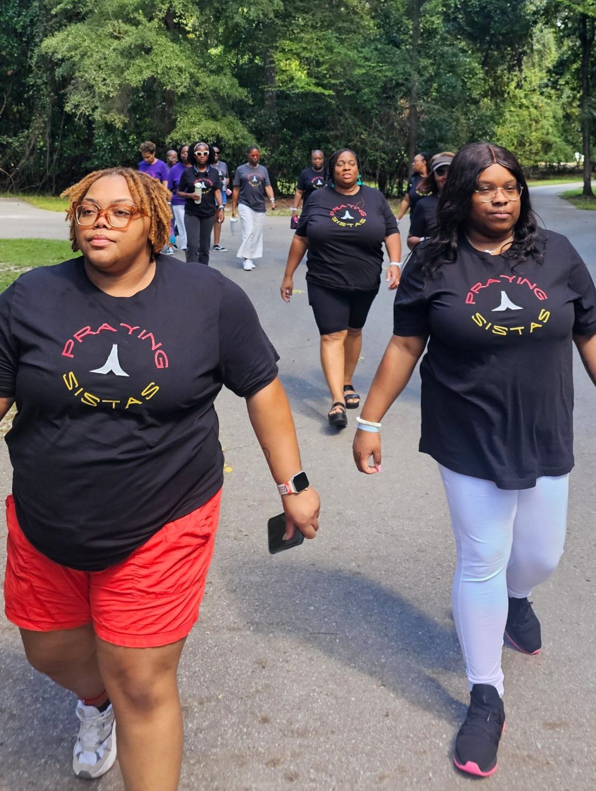 A group of women walking together outdoors in matching black Praying Sistas t-shirts
